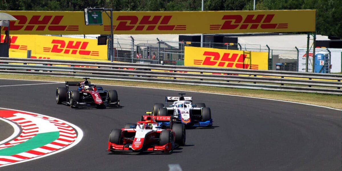 Formel-2-Rennwagen auf einer Rennstrecke, Seitenansicht, mit Team im Hintergrund