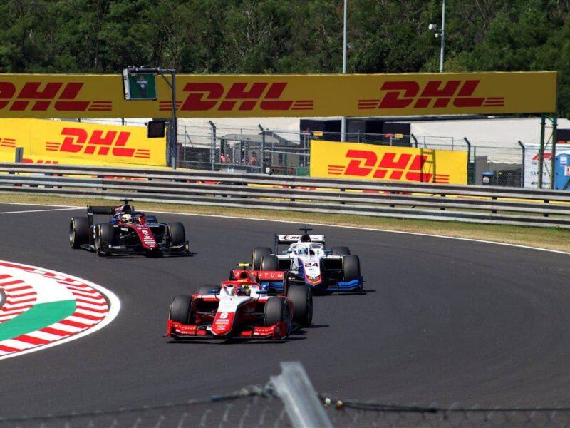 Formel-2-Rennwagen auf einer Rennstrecke, Seitenansicht, mit Team im Hintergrund