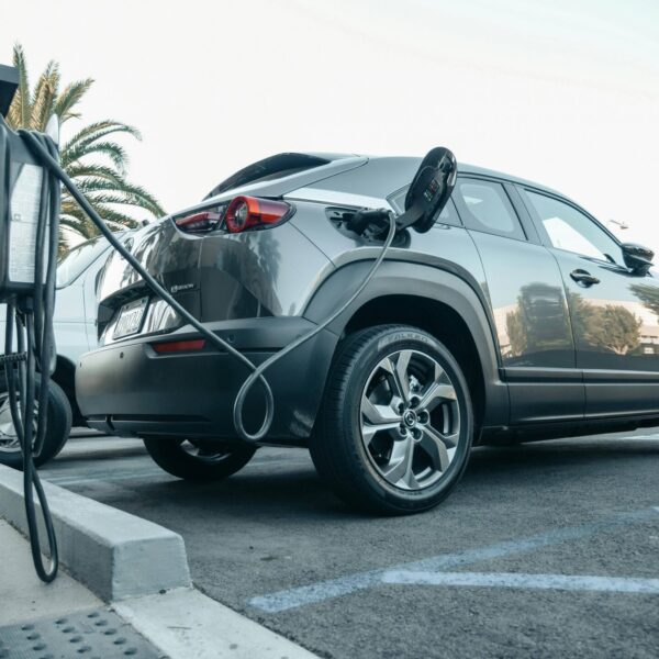 Symbolfoto: Mitarbeitende laden ein Elektroauto an einer Ladesäule des Unternehmens auf